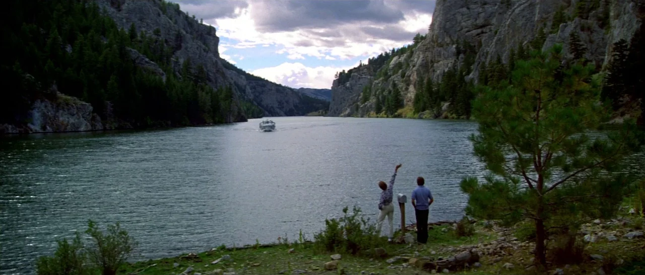 Thunderbolt & Lightfoot (1974) movie still: wide — A wide river flows through a rocky canyon with steep, evergreen-lined cliffs. Two people stand on…