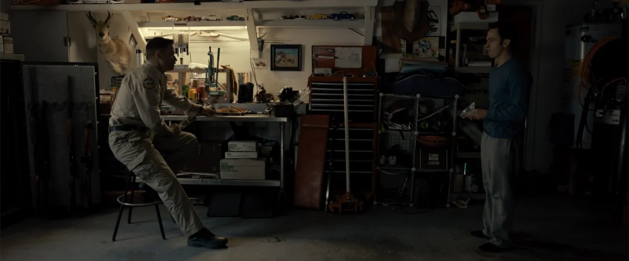 Frontera (2014) movie still: medium — A cluttered garage contains a workbench with tools, hunting trophies, and various household storage boxes. A…