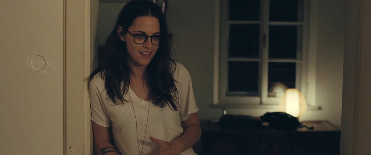 Clouds of Sils Maria (2014) movie still: medium — A woman stands in a dimly lit doorway with off-white walls. She leans against the frame while…