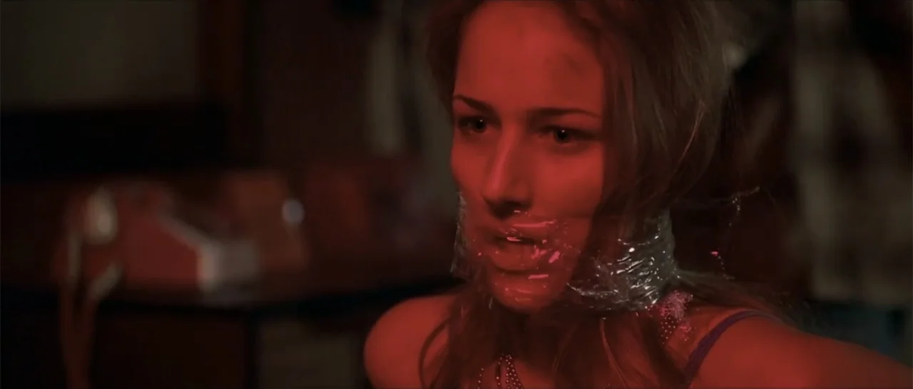 Joy Ride (2001) movie still: closeup — A dimly lit indoor space features a woman held captive in red light. She has clear plastic tape wrapped…