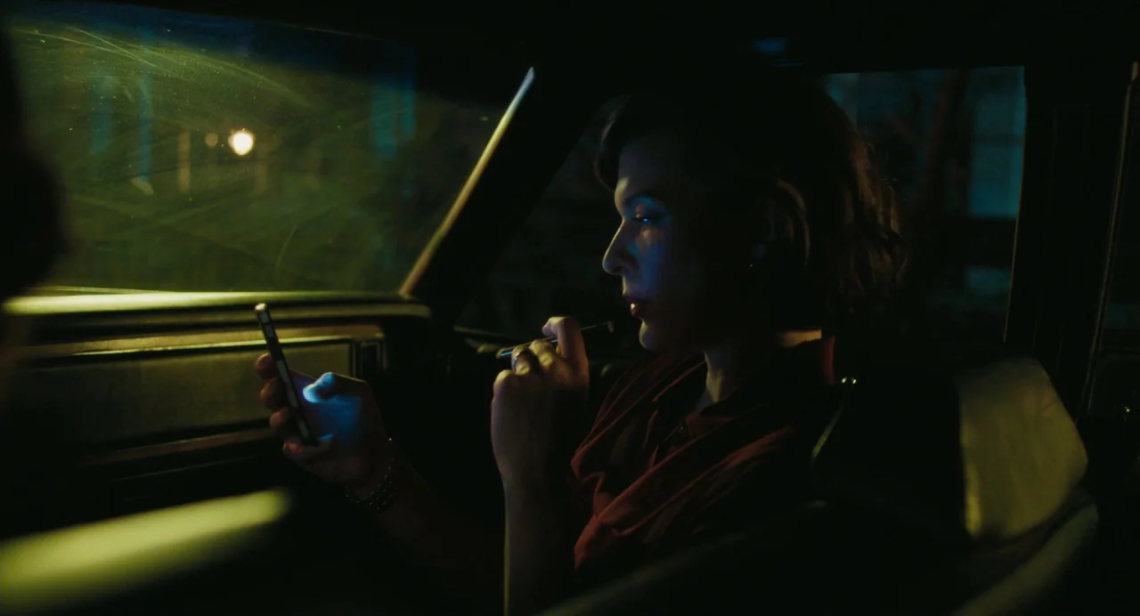 Cymbeline (2014) movie still: medium — The interior of a vehicle at night is dark with visible windshield streaks. A woman sits in the passenger…