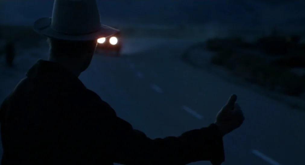 Bound For Glory (1976) movie still: medium — A dark, empty highway stretches through a dim night desert landscape. A man in a dark coat and hat…