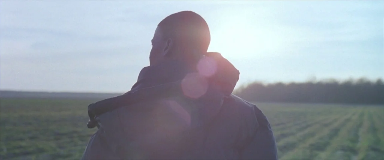 Ballast (2008) movie still: medium — A vast, flat agricultural field stretches toward a distant line of low trees. A man viewed from behind stands…