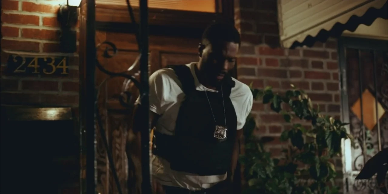 Equal Standard (2021) movie still: medium — A man stands on a residential porch illuminated by warm interior light. Brick siding and a house number…