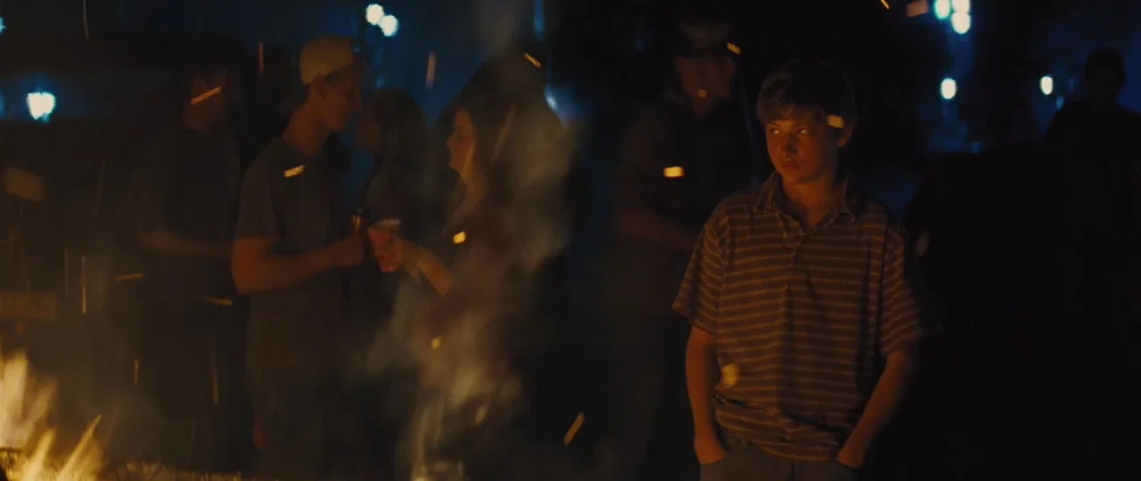Mud (2012) movie still: medium — A nighttime outdoor gathering features a group of teenagers standing near a glowing fire. A young boy in the…