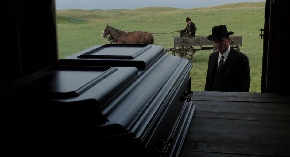Legends of the Fall (1994) movie still: wide — A wooden wagon sits in a vast, rolling green prairie under a grey sky. A black coffin rests in the…