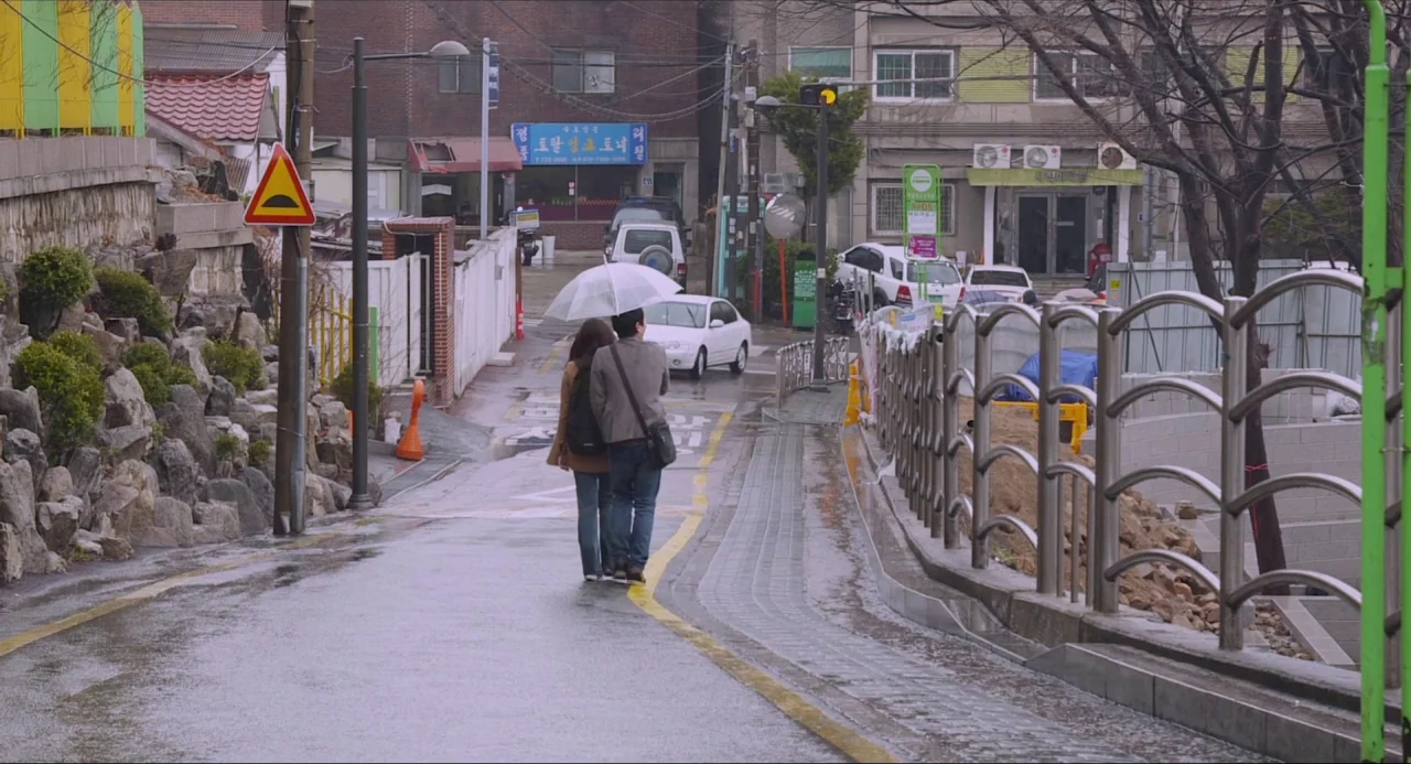 Nobody’s Daughter Haewon (2013) movie still: wide — A wet, narrow residential street in a South Korean urban neighborhood during daytime overcast…