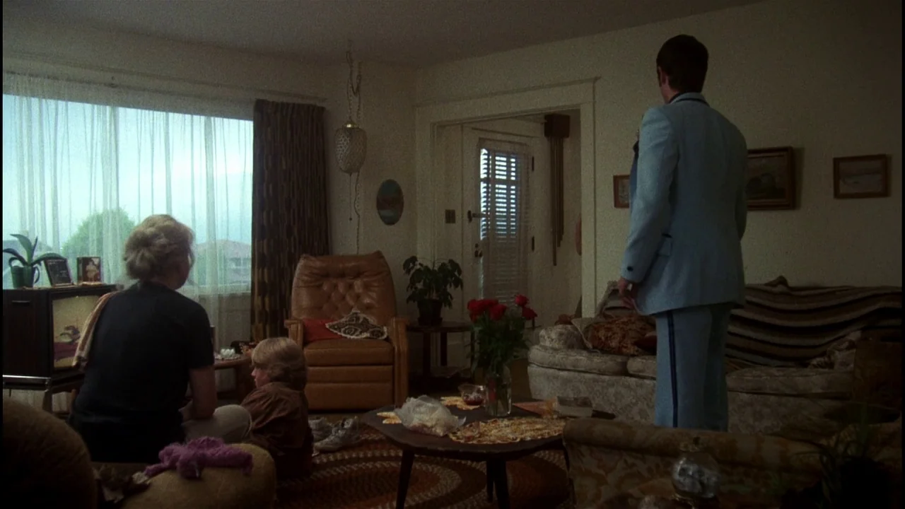 Star 80 (1983) movie still: wide — A residential room features 1970s decor including a brown leather recliner and patterned carpet. A family sits…