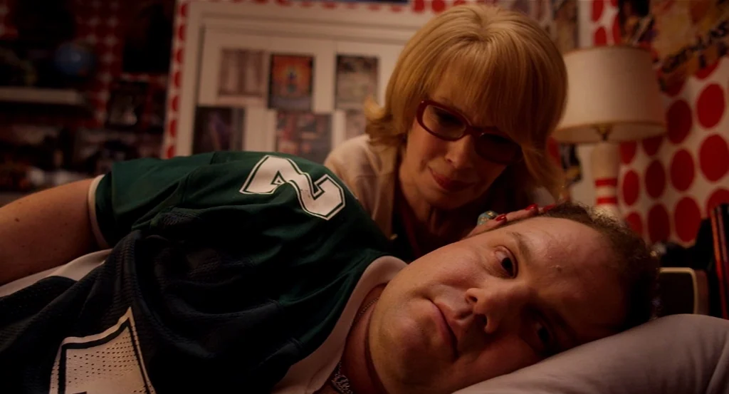 Dark Horse (2011) movie still: medium — A bedroom features dark red wallpaper with white polka dots and posters on the walls. A blonde woman with…