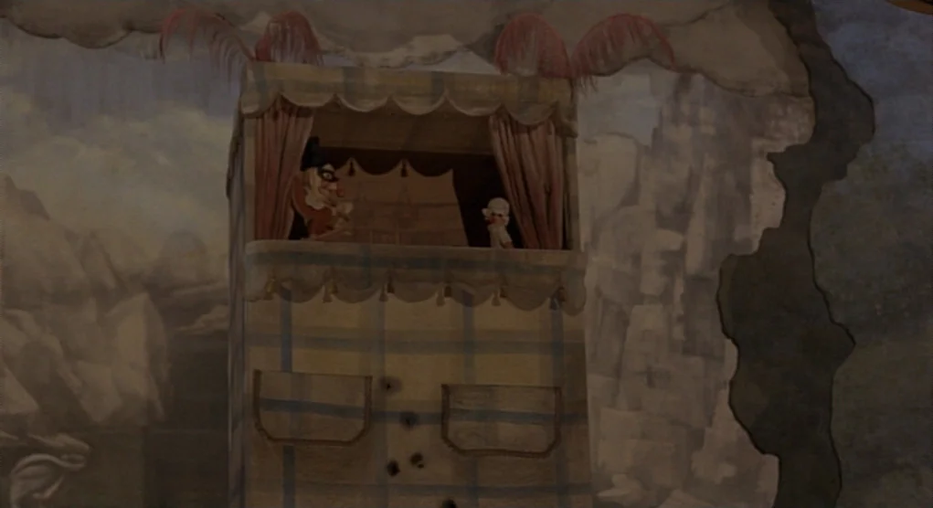 Time Bandits (1981) movie still: medium — A miniature fabric puppet theater sits before a painted backdrop of jagged mountains. Two small puppets…