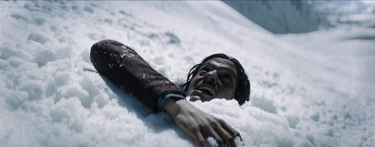 Society of the Snow (2023) movie still: medium — A vast, white, sunlit slope of snow covers the entire frame. A man's head and arm emerge from the…