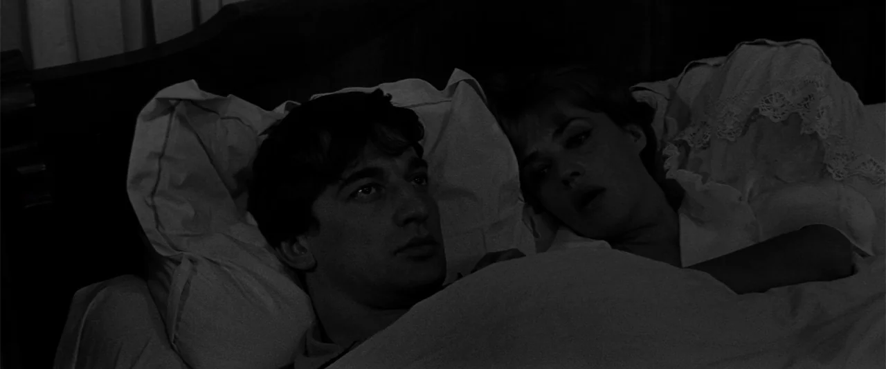Jules and Jim (1962) movie still: medium — A dark bedroom with two people lying in a bed under white linens. A man and a woman face one another…