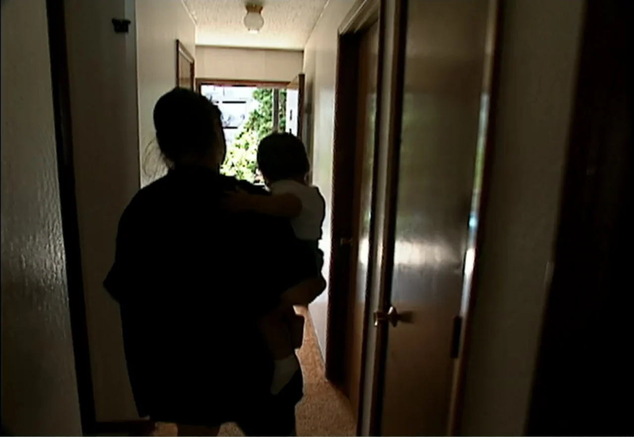 Broken Child (2000) movie still: medium — An interior apartment hallway features beige walls and a patterned carpet floor. A person stands facing…