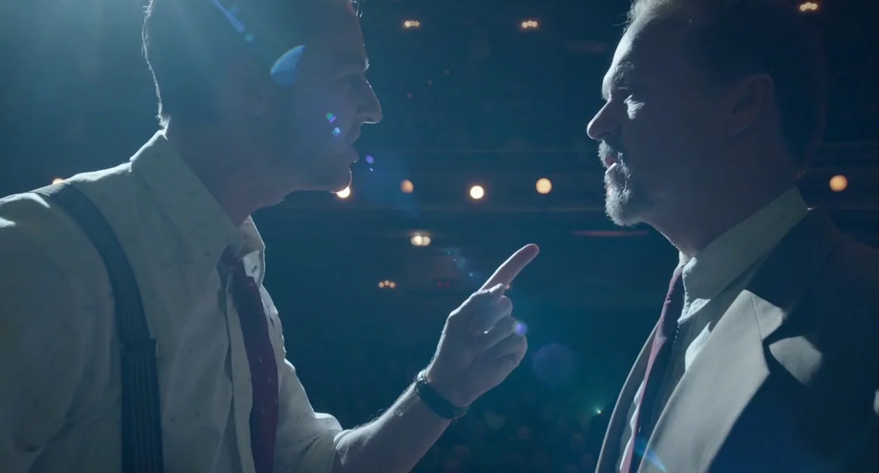 Birdman (2014) movie still: medium — A dimly lit theater stage has rows of dark, out-of-focus seating in the background. Two men in formal attire…
