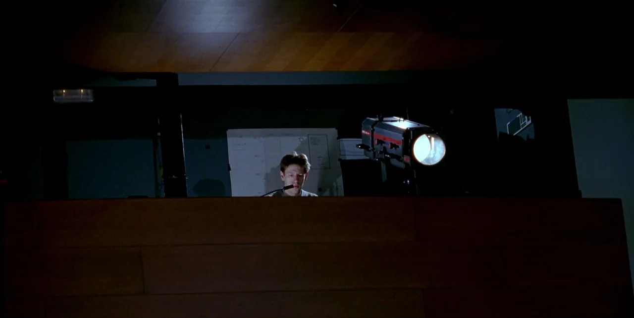 The Flower of My Secret (1995) movie still: wide — A dark projection booth with wooden walls and a large, visible spotlight fixture. A man sits at a…