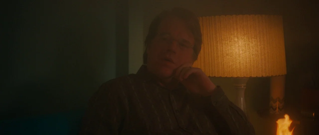 Synecdoche, New York (2008) movie still: medium — A dimly lit interior space filled with haze and warm directional lighting. A man sits beside a…