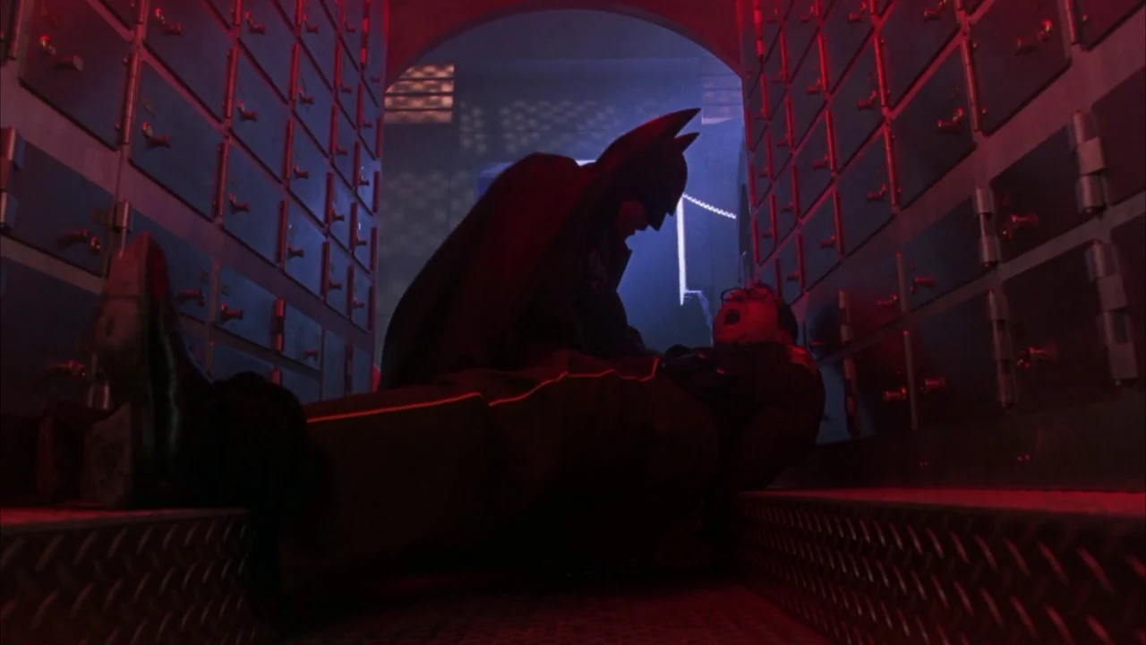 Batman Forever (1995) movie still: medium — A narrow vault corridor is lined with rows of small metal safety deposit boxes. A costumed hero looms…