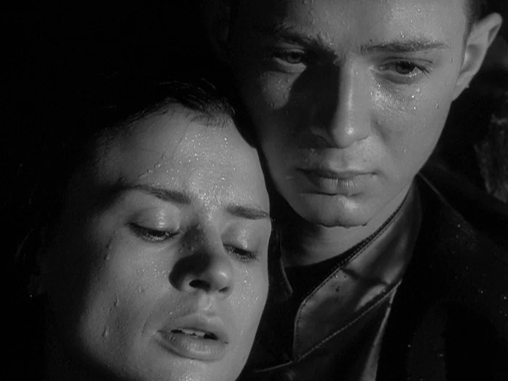 Through A Glass Darkly (1961) movie still: closeup — A close-up shot depicts two young individuals huddled together under rainy conditions. Water…