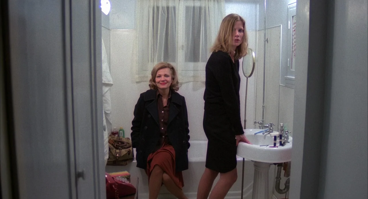 Opening Night (1977) movie still: fullbody — A sterile residential bathroom featuring white tiled walls and a pedestal sink. One woman sits on the…