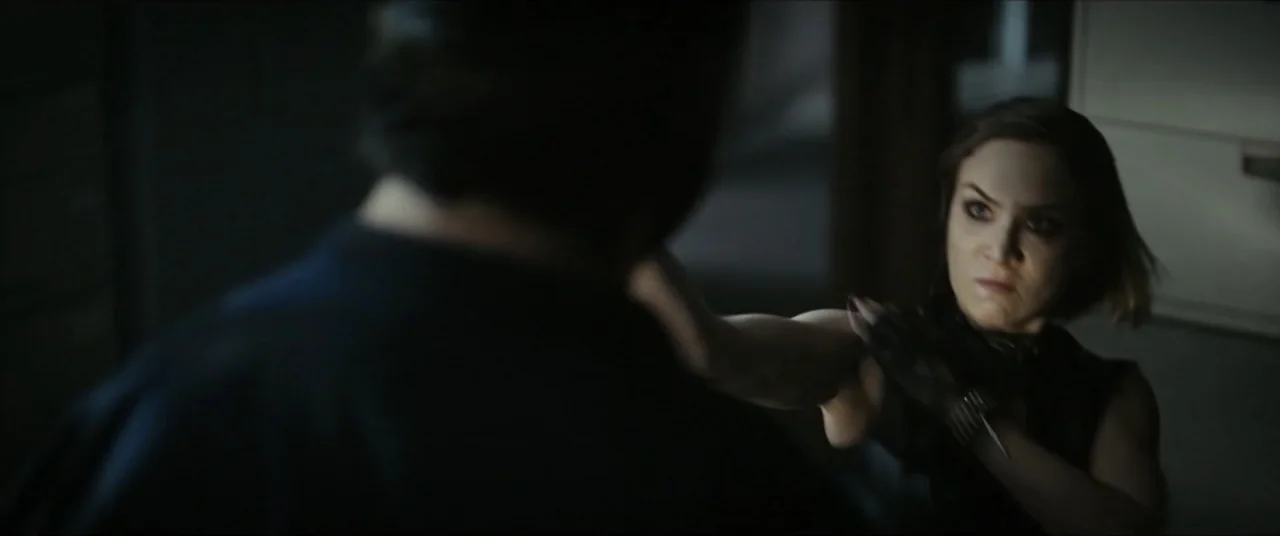Vicious Fun (2021) movie still: medium — A dark indoor space with blurred architectural lines in the background. A woman in a black top strikes a…