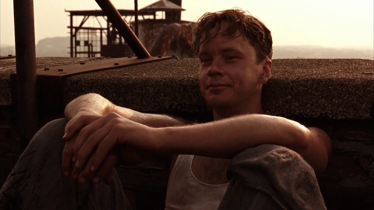 The Shawshank Redemption (1994) movie still: medium — A flat gravel roof features a metal railing and industrial structures in the distance. A man…