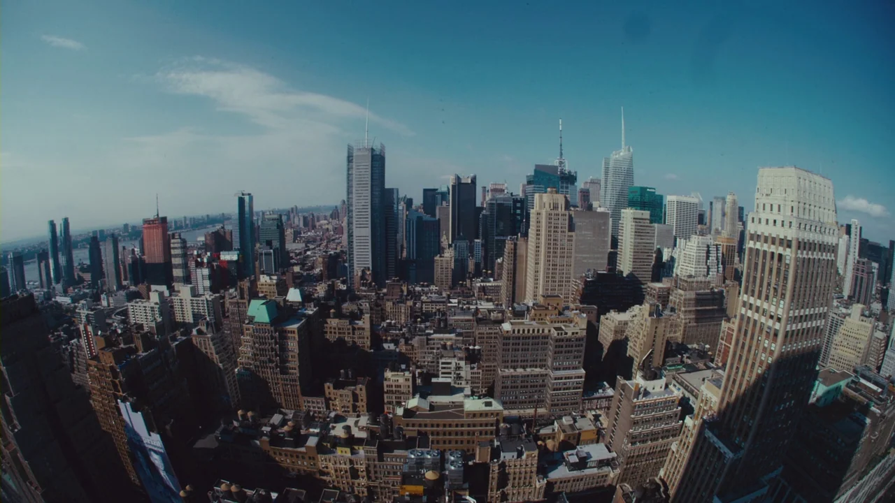 Margin Call (2011) movie still: establishing — An expansive aerial view of the New York City skyline under a clear sky. Dense skyscrapers fill the…