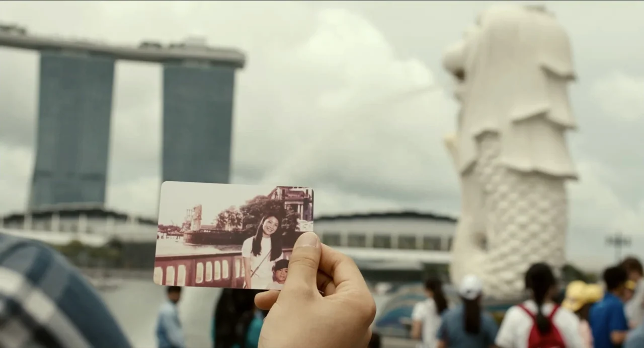 Ramen Shop (2018) movie still: closeup — A person holds a small, aged photograph featuring two individuals in front of a monument. The background…