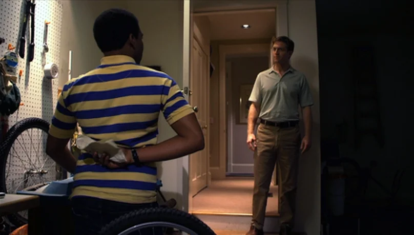 Mystery Team (2009) movie still: medium — A cluttered residential garage features a pegboard wall with tools and a bicycle wheel. A young man stands…