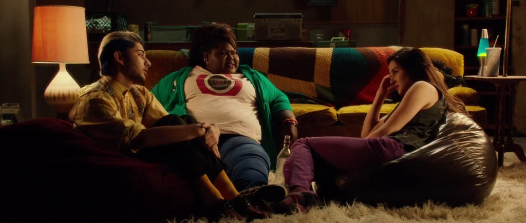 White Bird in a Blizzard (2014) movie still: medium — A dimly lit room contains a colorful knit blanket draped over a sofa. Three young adults…