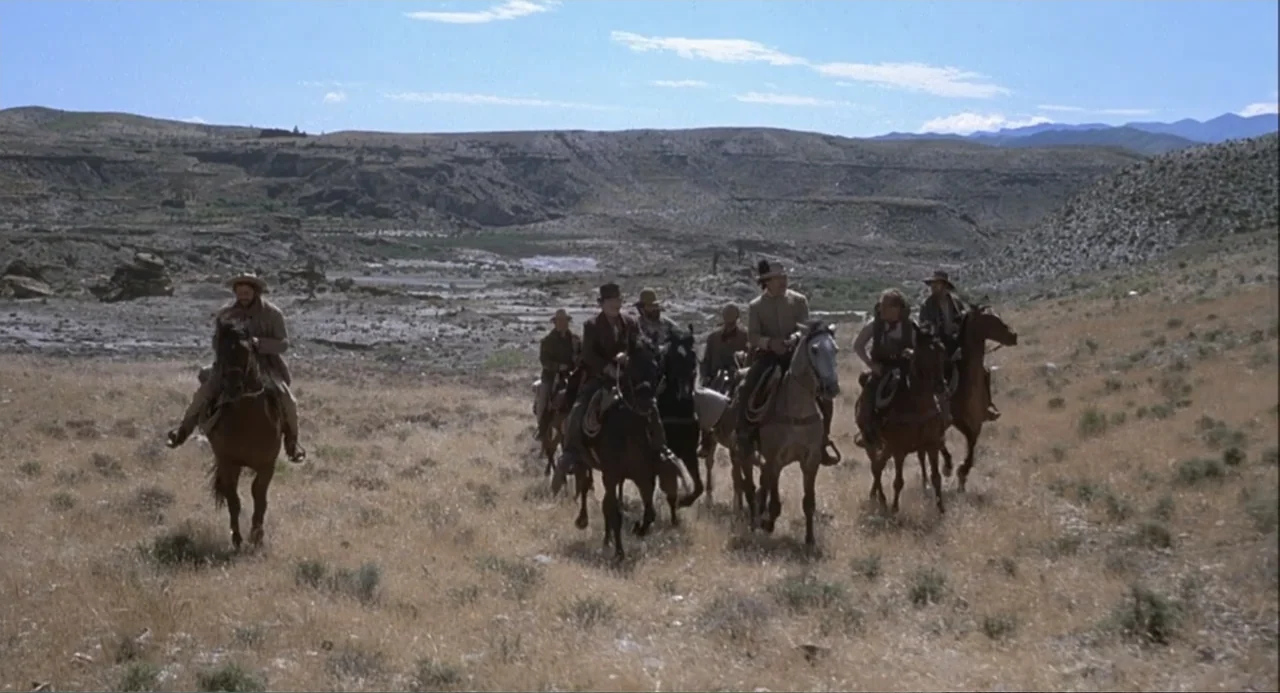 Chato's Land (1972) movie still: wide — A vast, dry desert landscape stretches out beneath a wide, clear blue sky. A small group of men on horseback…