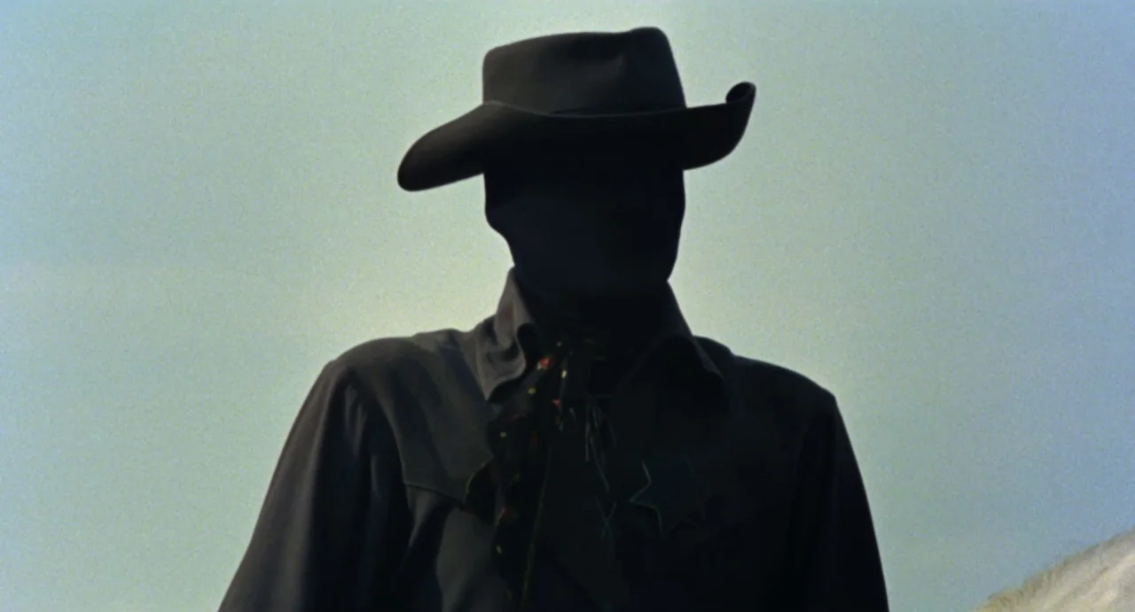 Johnny Colt (1966) movie still: medium — An open outdoor space under a bright, cloudless sky. A silhouetted figure wearing a cowboy hat stands…