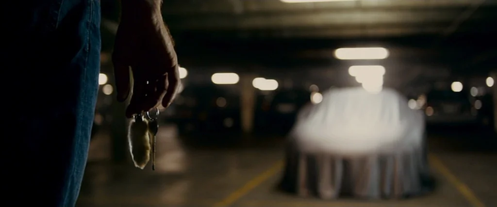 MacGruber (2010) movie still: closeup — A dark subterranean concrete parking structure features rows of dimly lit parking spots. In the foreground,…