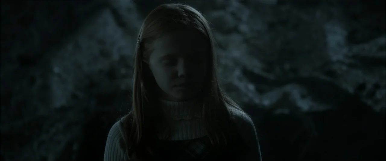 The Hollow Child (2018) movie still: closeup — A dark rocky cave interior features rough stone walls and low lighting. A young girl with long hair…