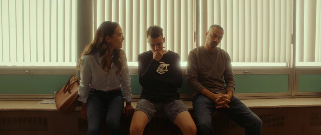 Random Acts of Violence (2019) movie still: medium — A window-lit waiting area with vertical blinds and a teal-painted wall section underneath.…