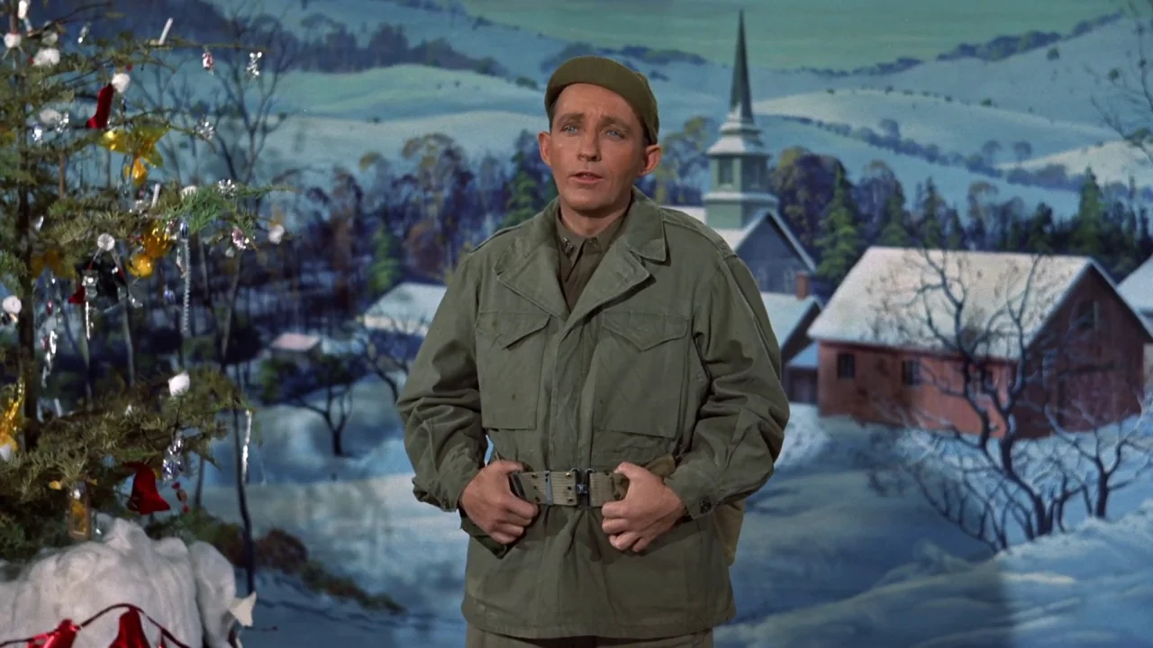 White Christmas (1954) movie still: medium — A man stands in front of a painted theatrical backdrop depicting a snowy village. The scene includes a…