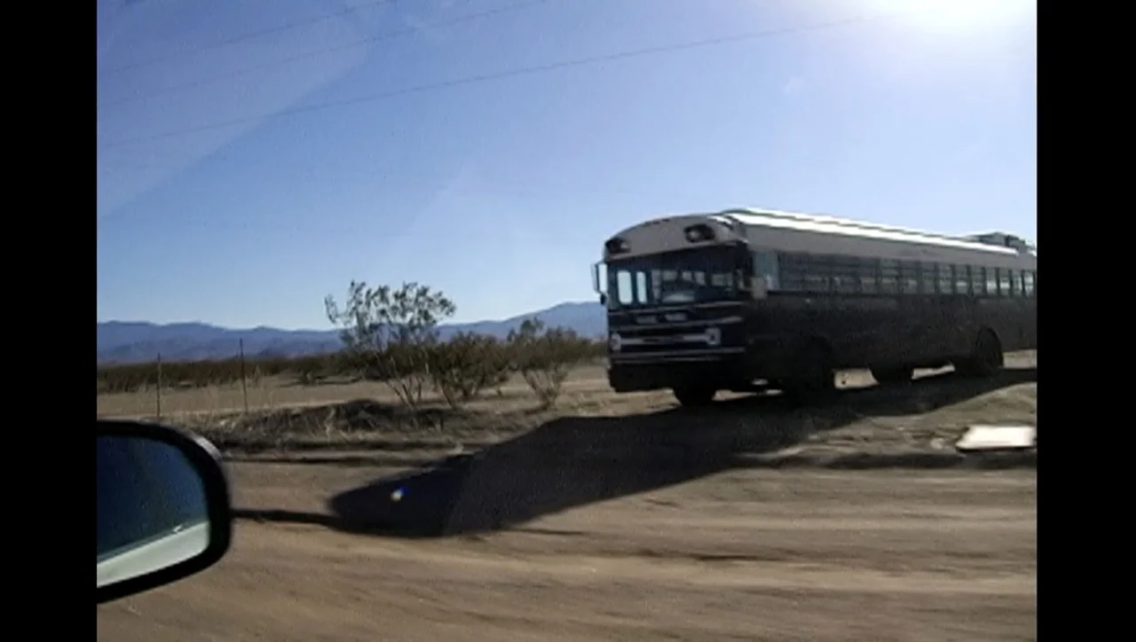 The Trials of Ted Haggard (2009) movie still: wide — A flat desert landscape features a dark passenger bus parked near a dirt road. In the…