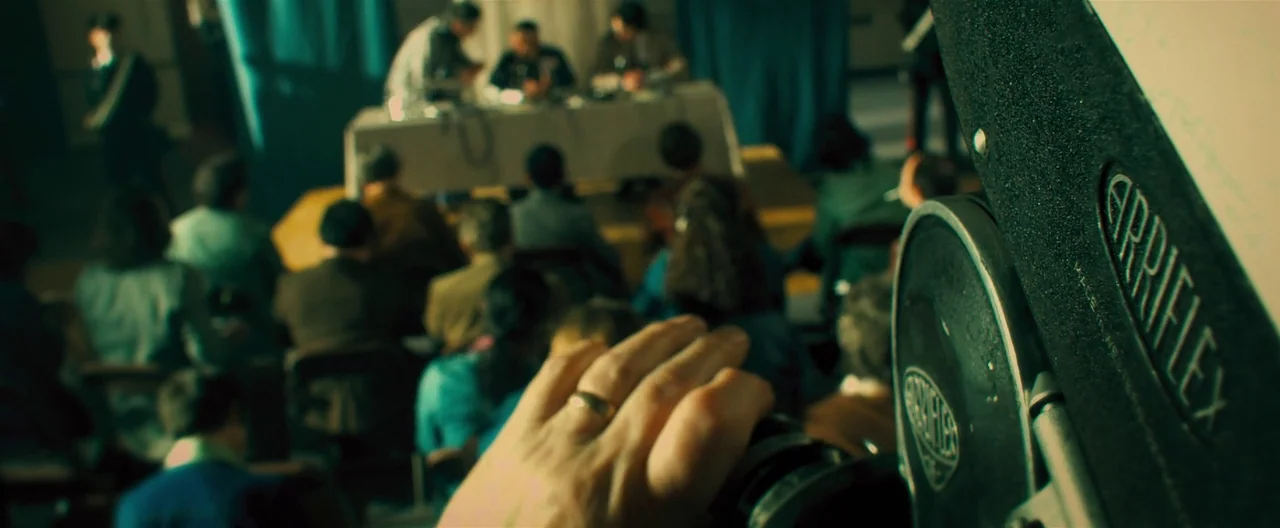 Rush (2013) movie still: medium — A crowded press conference room features a long table with speakers at the front. A camera operator records the…