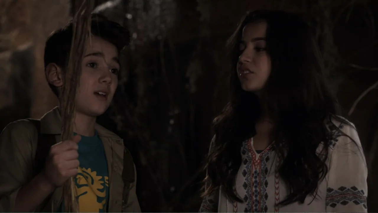 Legends of the Hidden Temple (2016) movie still: medium — A dark, dimly lit environment features rock formations in the background. A young boy…