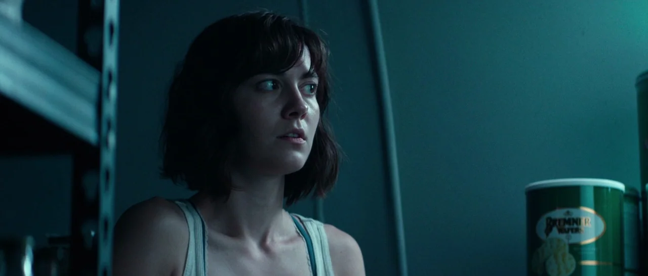 10 Cloverfield Lane (2016) movie still: medium — A dimly lit storage area features dark metallic shelving and a container of wafers. A young woman…