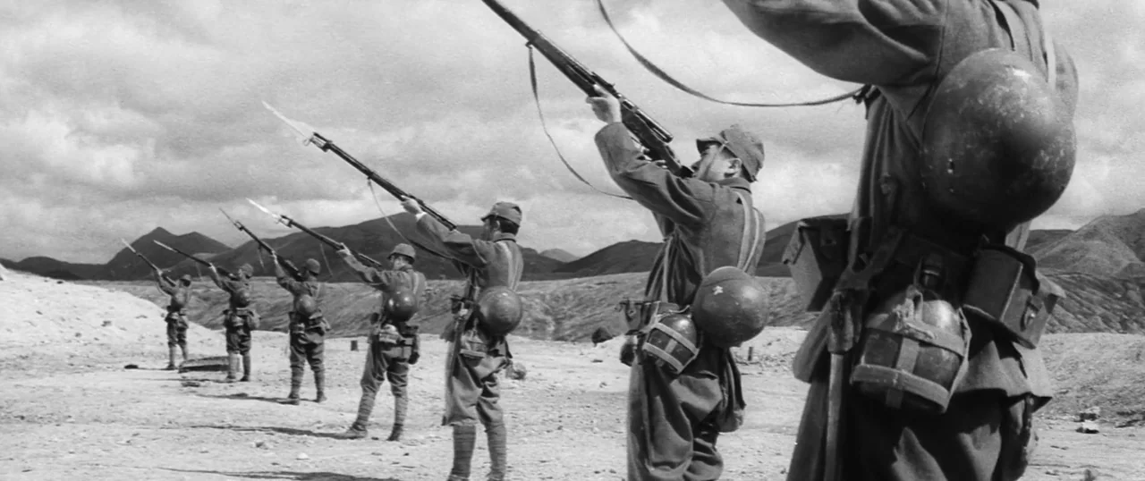 The Human Condition I: No Greater Love (1959) movie still: wide — A line of soldiers in uniform stands on a dry, rocky expanse aiming rifles.…