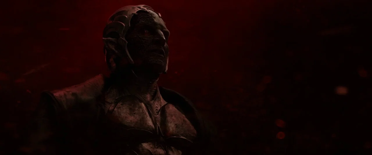 Thor: The Dark World (2013) movie still: medium — A humanoid figure stands against a dark, red-lit void filled with indistinct particles. The…