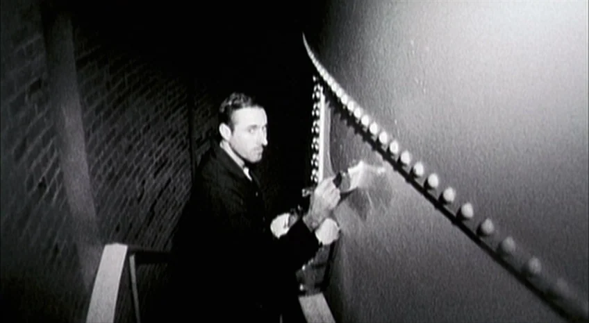Brand Upon the Brain! (2006) movie still: medium — A dark stairwell features a brick wall adjacent to a large curved structure. A man in a dark coat…