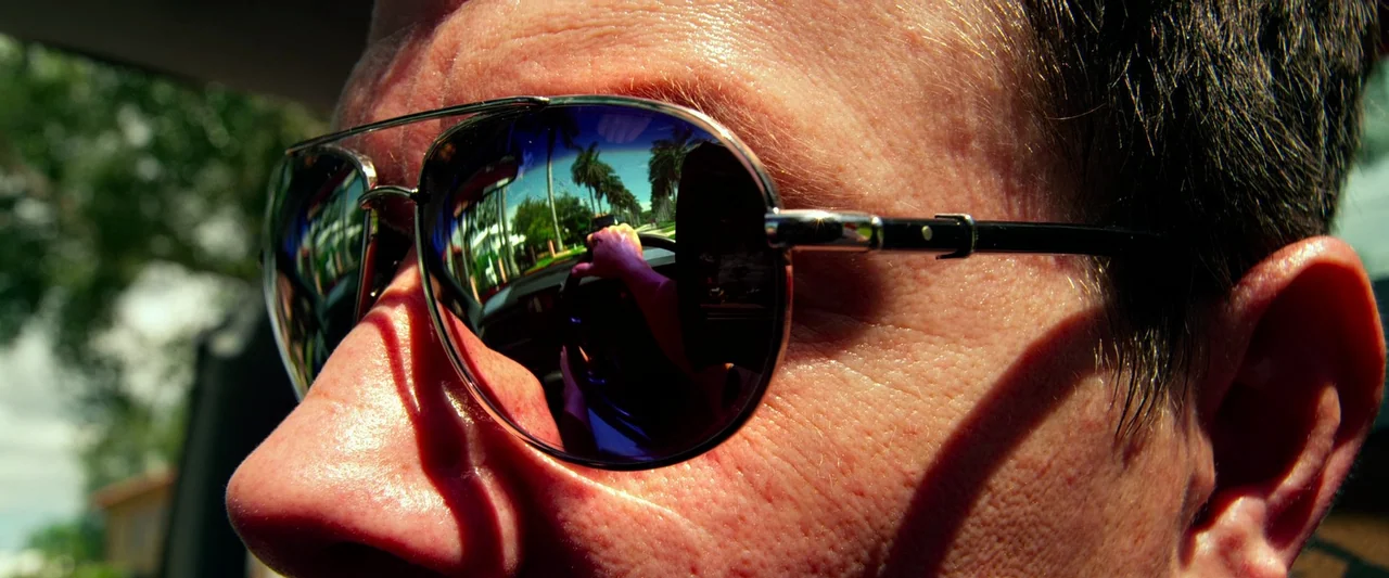 Pain & Gain (2013) movie still: closeup — A close-up view of a man's face while driving in bright daylight. The lenses of his aviator sunglasses…