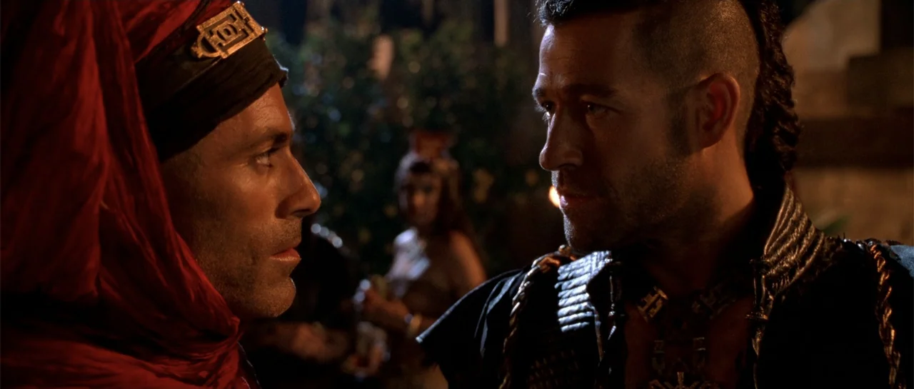 The Scorpion King (2002) movie still: medium — A dark indoor space contains two men positioned closely to one another. The men are dressed in ornate…
