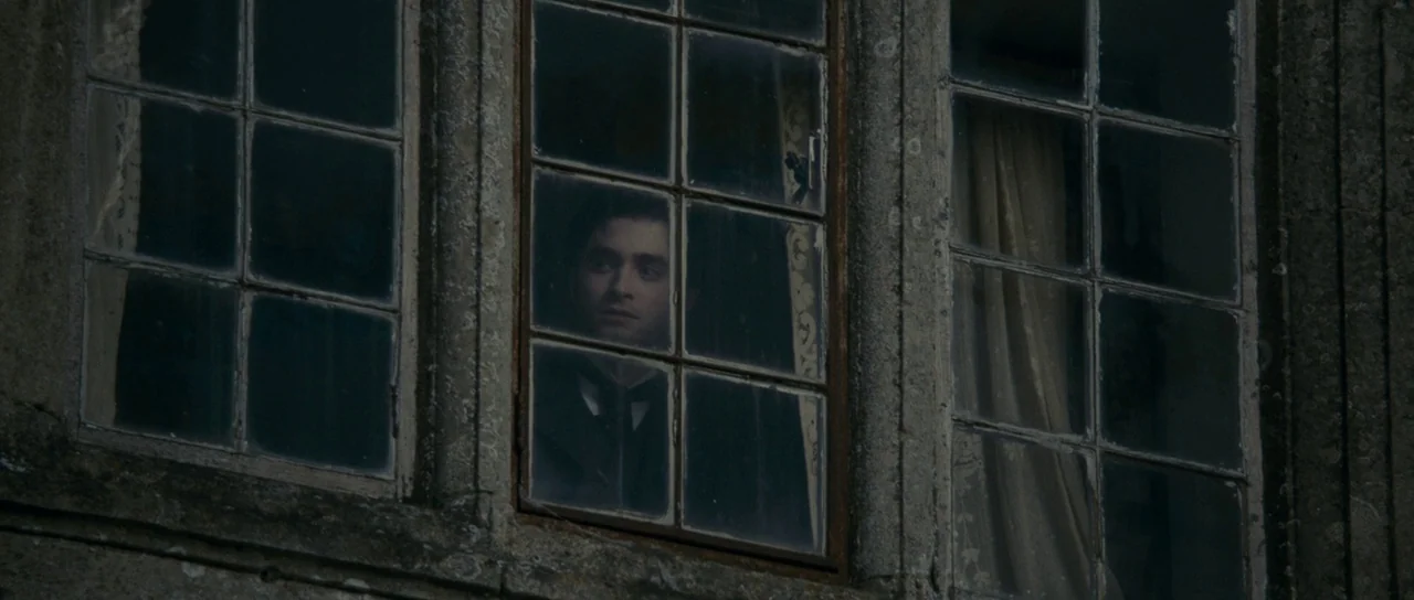 The Woman in Black (2012) movie still: medium — The exterior stone wall of an old house features three glass paneled window frames. A man looks…