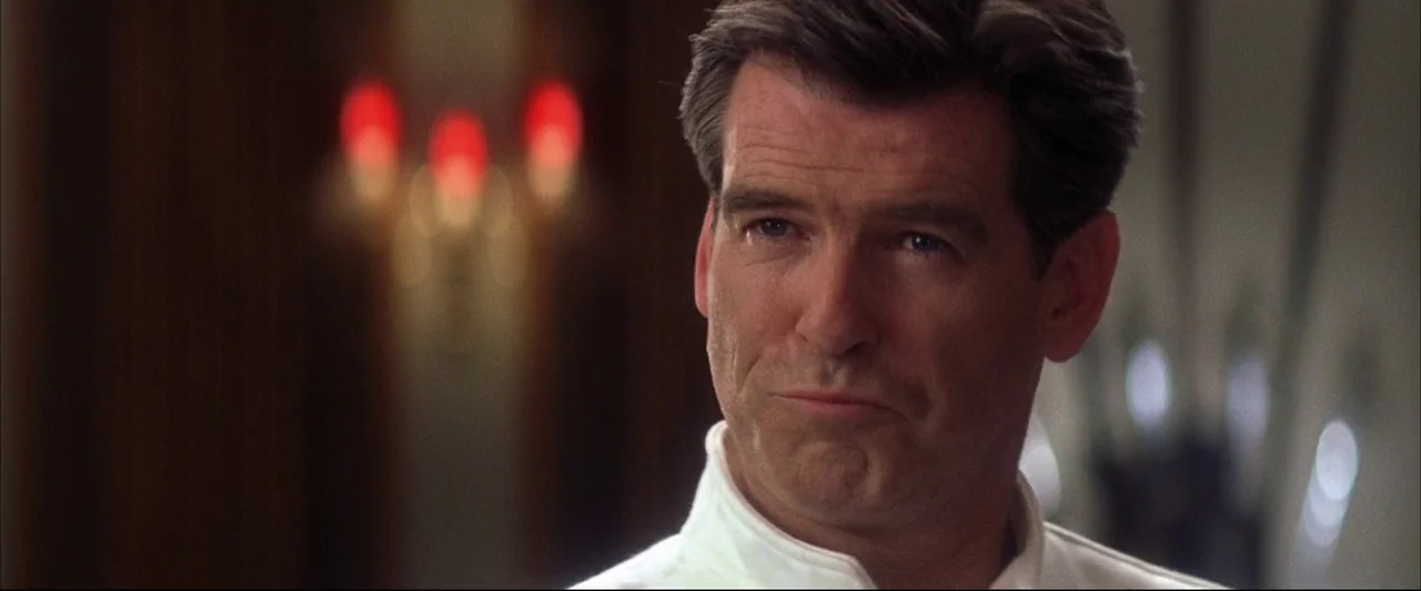 Die Another Day (2002) movie still: closeup — An interior space with dark walls and blurry red lights in the background. A man stands in the…