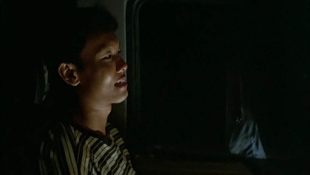 Tropical Malady (2004) movie still: medium — A dark vehicle interior with a view through a window into blackness. A young man sits in the passenger…