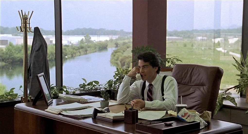 Sex, Lies And Videotape movie still: medium — A corner office space features floor-to-ceiling windows overlooking a canal and grassy landscape. A…