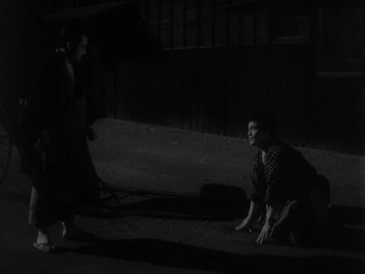 Sanshiro Sugata (1943) movie still: fullbody — A dark outdoor setting at night features a dirt path beside a wooden building. One man stands while…