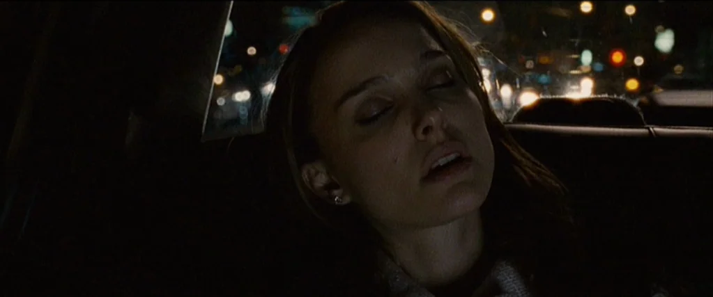 Black Swan (2010) movie still: closeup — The interior of a moving car at night shows a woman resting against glass. Blurred city lights appear…
